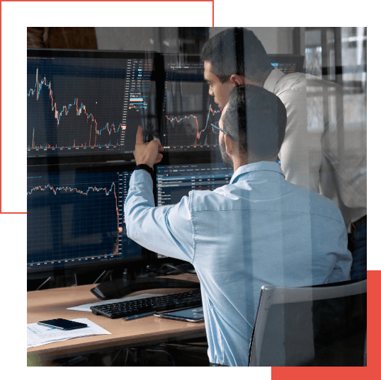  Two men analyze financial data displayed on multiple computer monitors, discussing market trends and leveraging Google Chronicle in an office setting.